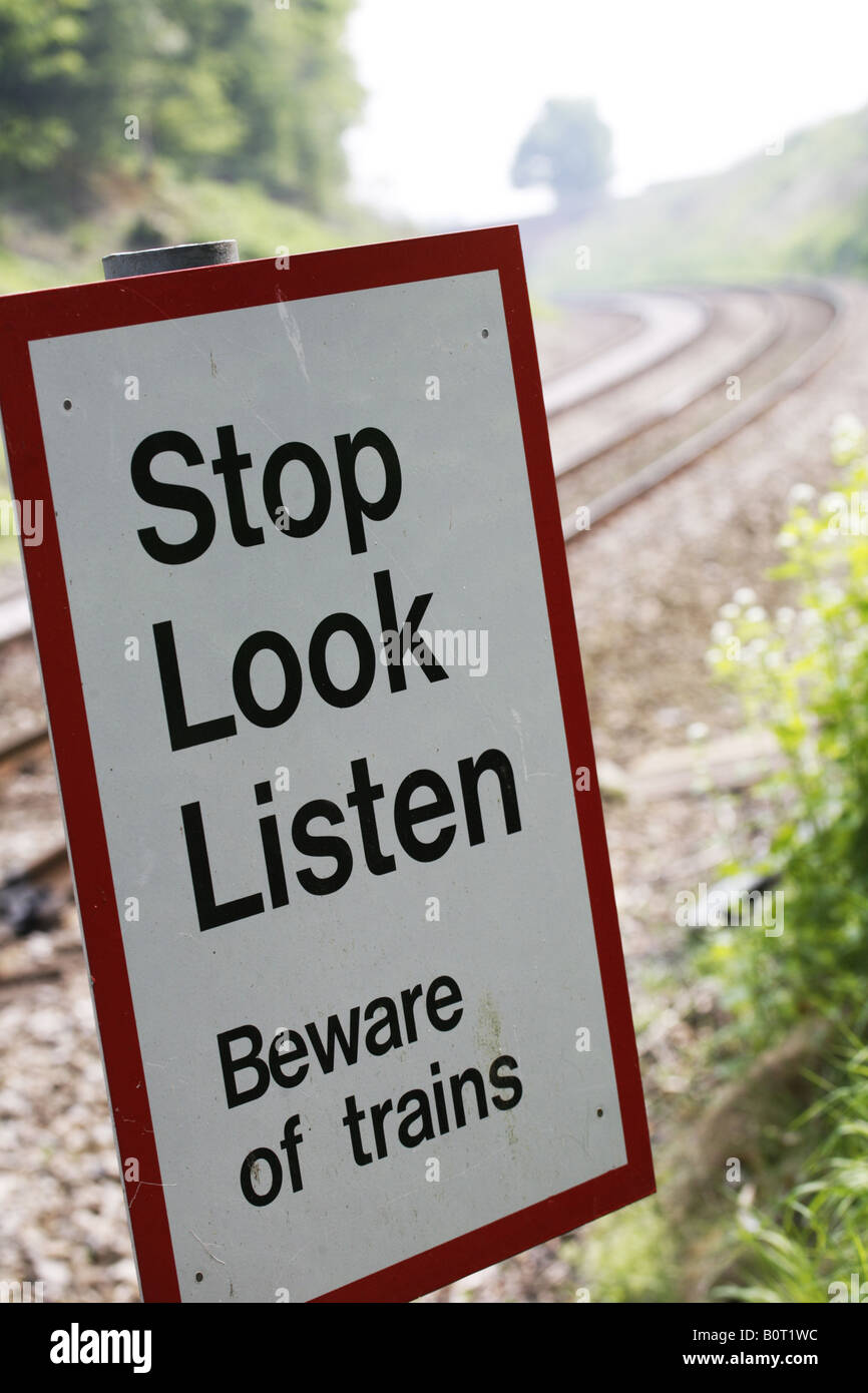 Smettere di guardare ascoltare attenti di treni segno a sentiero oltre le linee ferroviarie Foto Stock