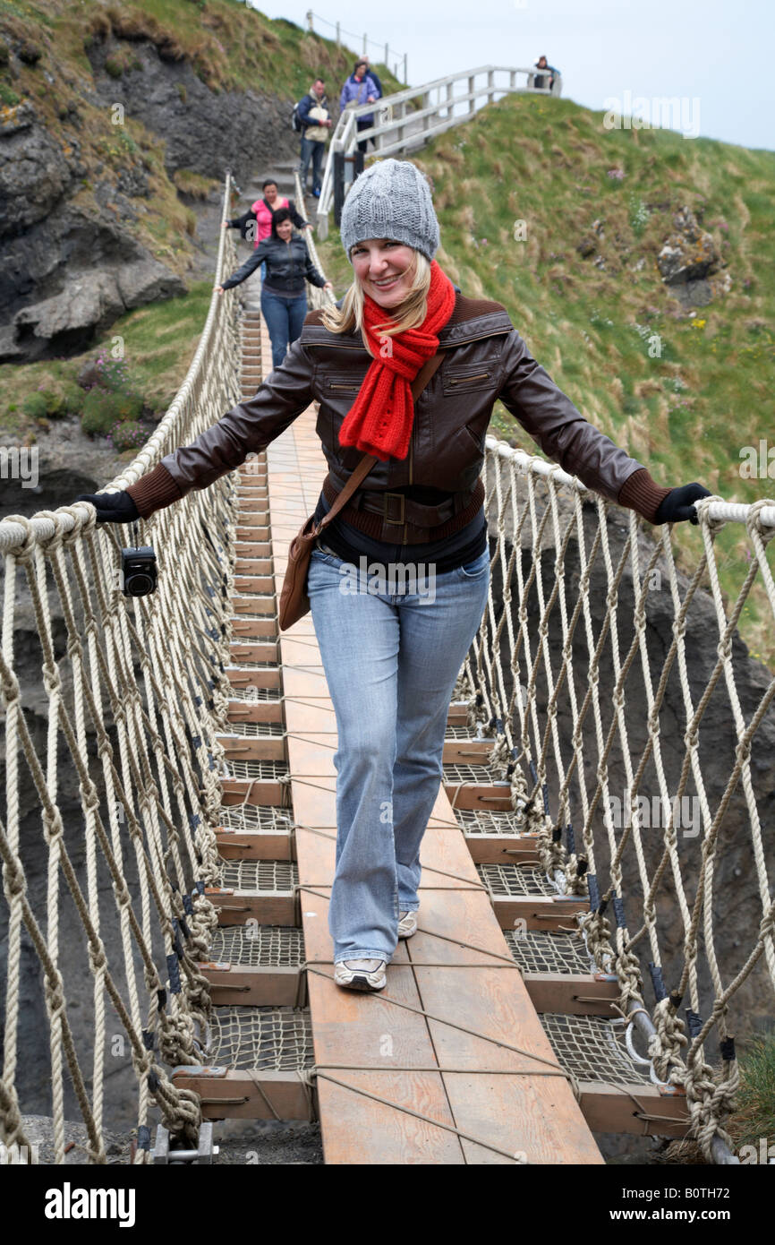 Femmina di turisti attraversando il carrick a rede ponte di corde sulla contea di Antrim coast Irlanda del Nord Foto Stock