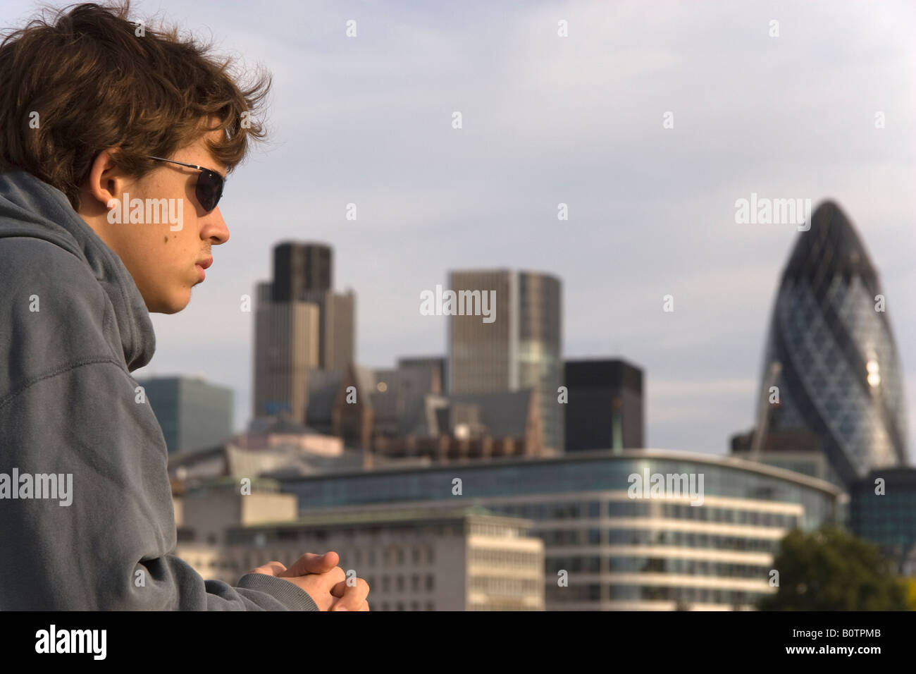 Ritratto di un ragazzo adolescente indossando occhiali da sole con torre 42 di Willis e cetriolino edifici visibili nella città di Londra sfocato Foto Stock