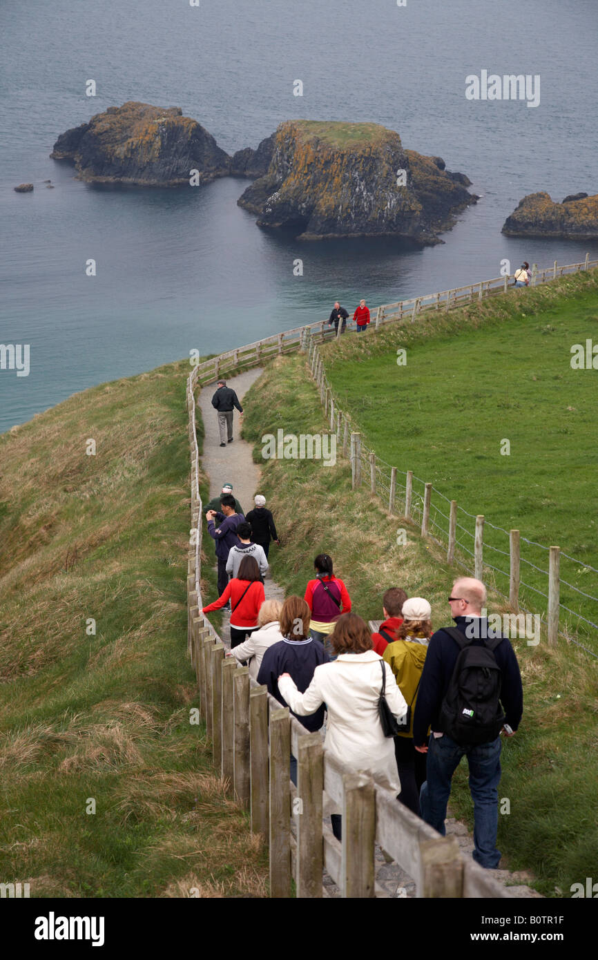 I turisti a piedi verso il basso il percorso lungo il carrick a rede ponte di corde sulla contea di Antrim coast Irlanda del Nord Foto Stock