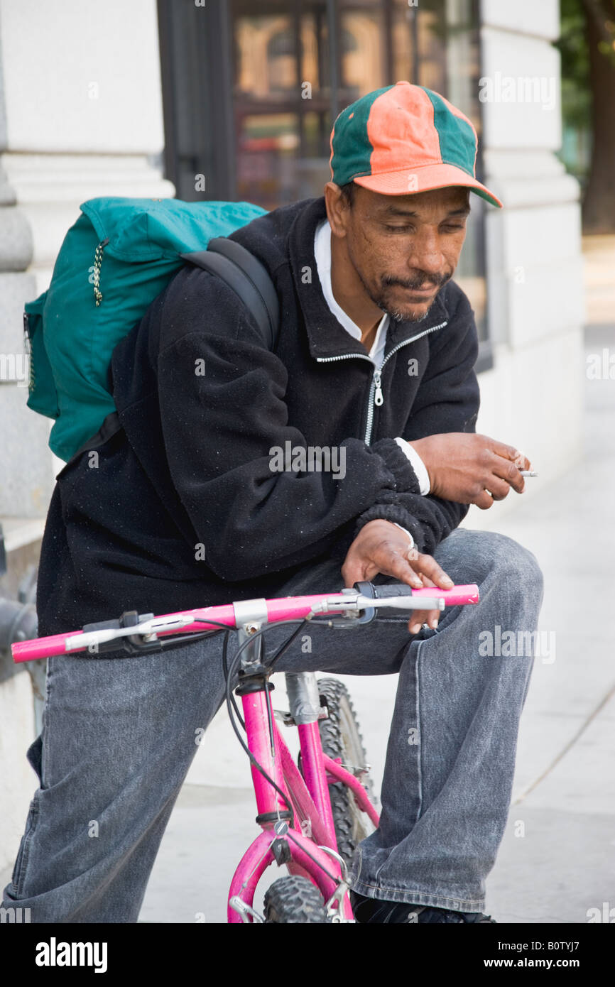 Senzatetto maschio su una bicicletta. indossare uno zaino. Foto Stock