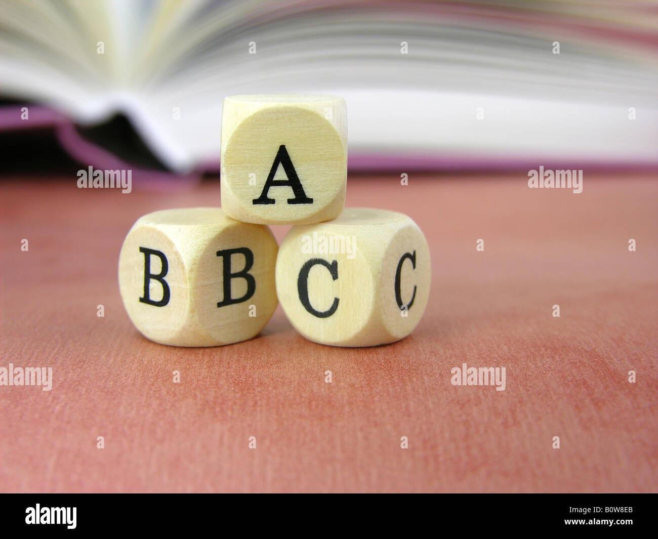 Tre dadi letterati ABC con libro aperto in background Foto Stock