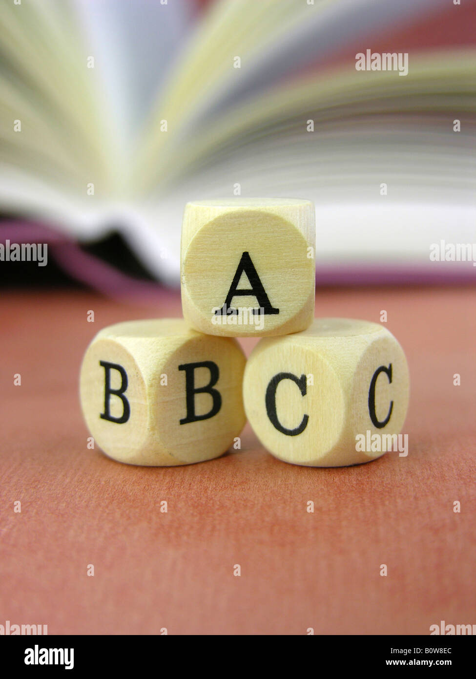 Tre dadi letterati ABC con libro aperto in background Foto Stock
