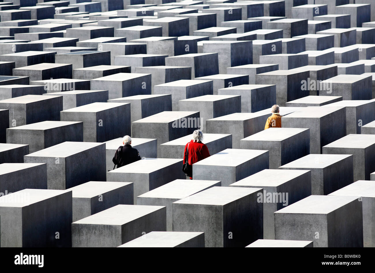 Tre persone vestite di rosso, nero e giallo-oro giacche a piedi tra le lastre di cemento del monumento commemorativo dell'Olocausto, Berlino, Germa Foto Stock