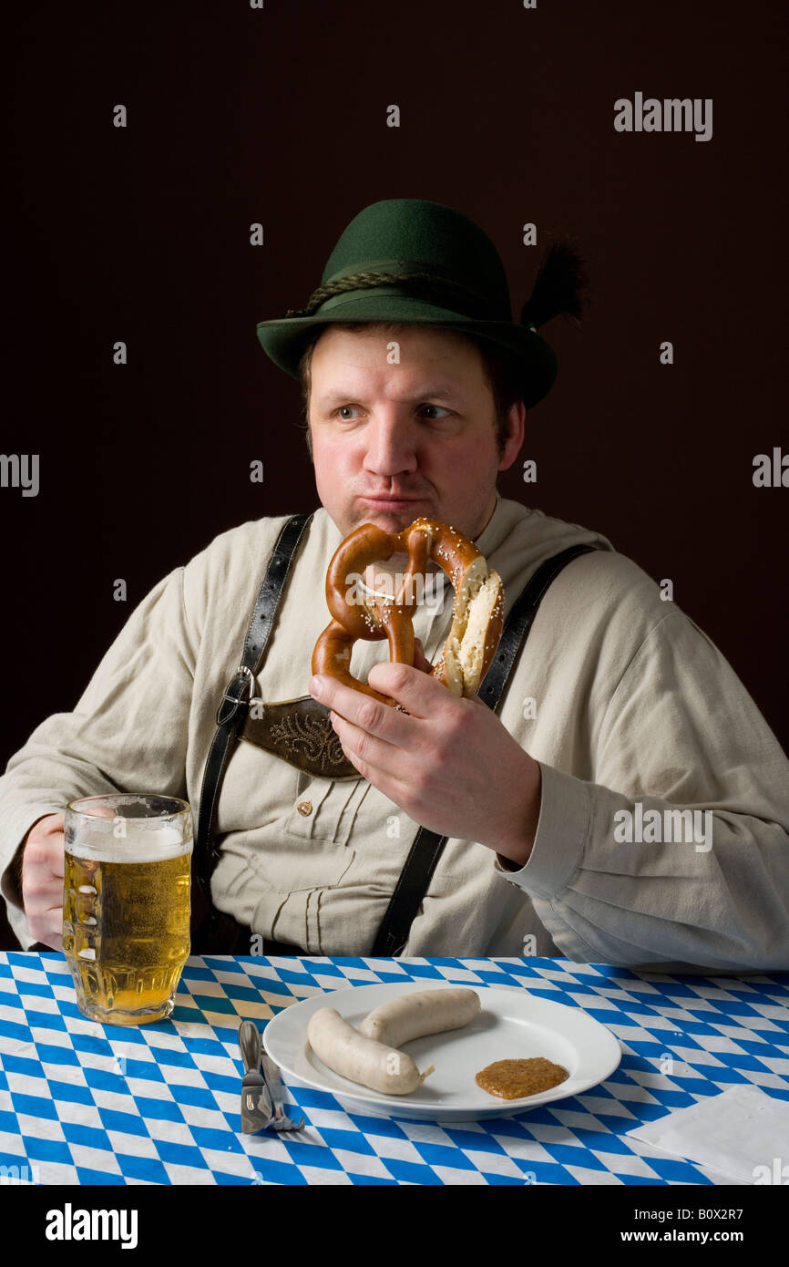 Stereotipi uomo tedesco in costume bavarese di mangiare un pretzel e bere una birra Foto Stock