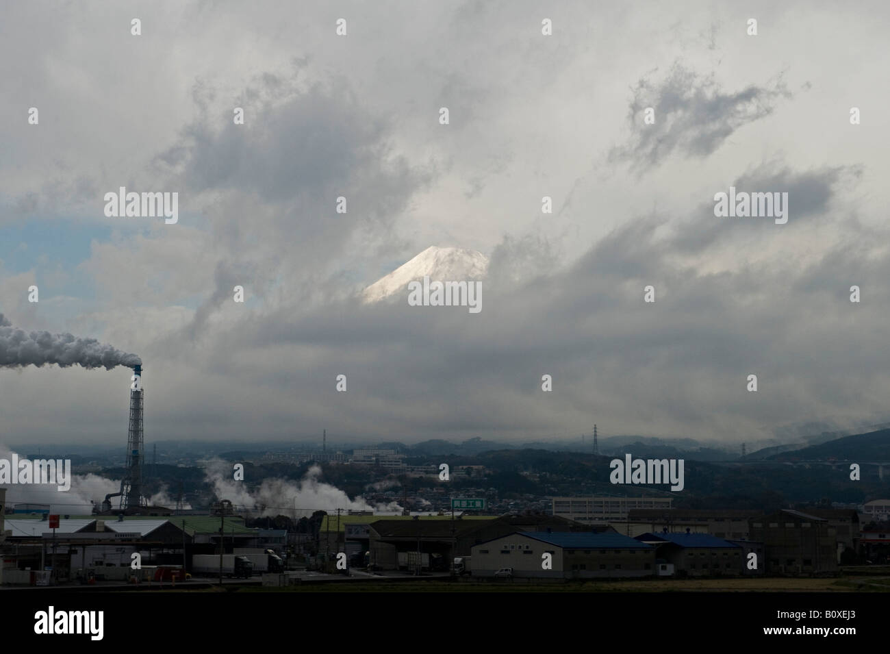 Giappone. Uno scorcio del Monte Fuji attraverso le nuvole, che torreggiano sul triste paesaggio industriale fuori Tokyo, visto dallo shinkansen o dal treno proiettile Foto Stock