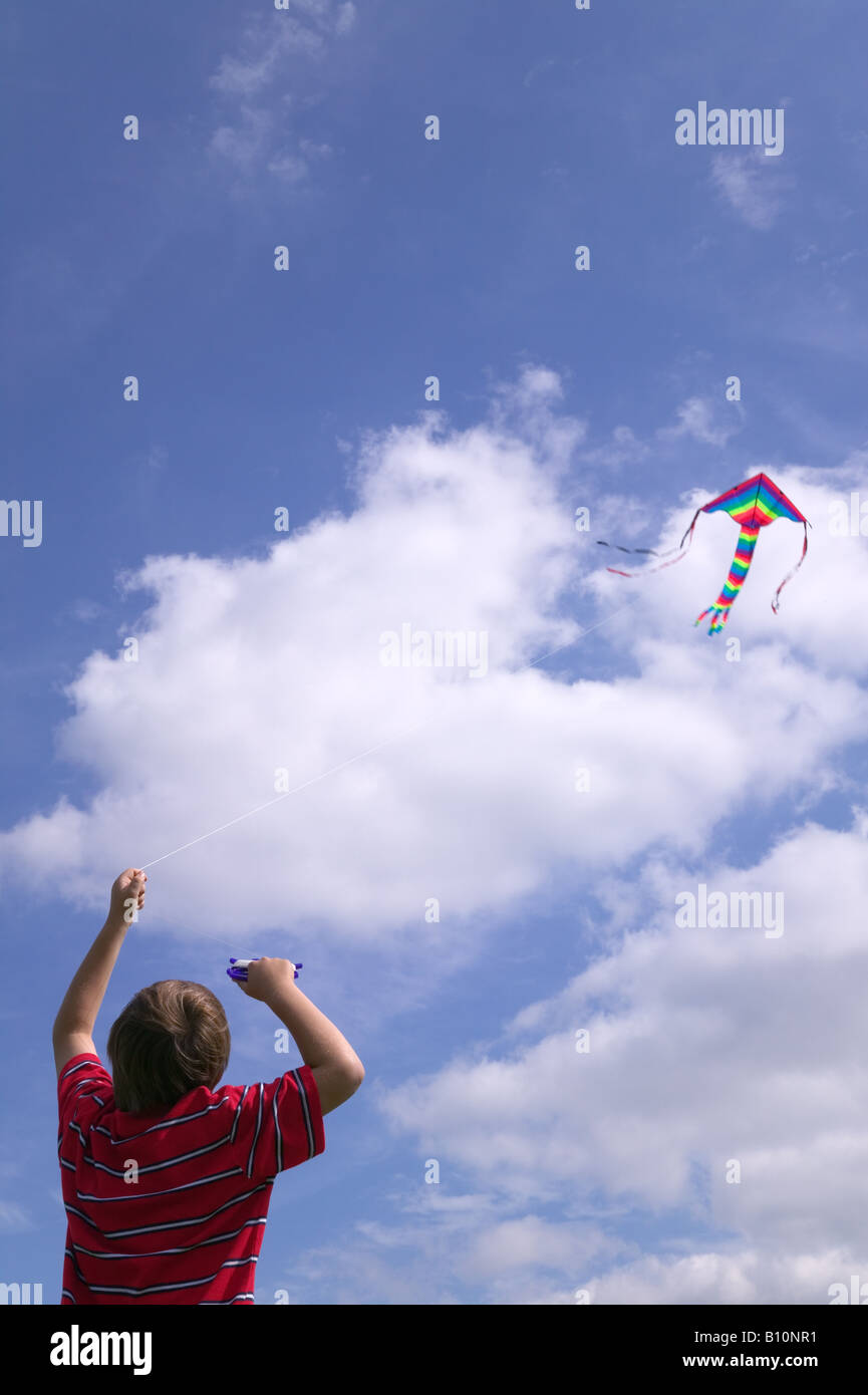 Ragazzo in una maglietta rossa battenti la sua kite in un brillante blu cielo nuvoloso Foto Stock