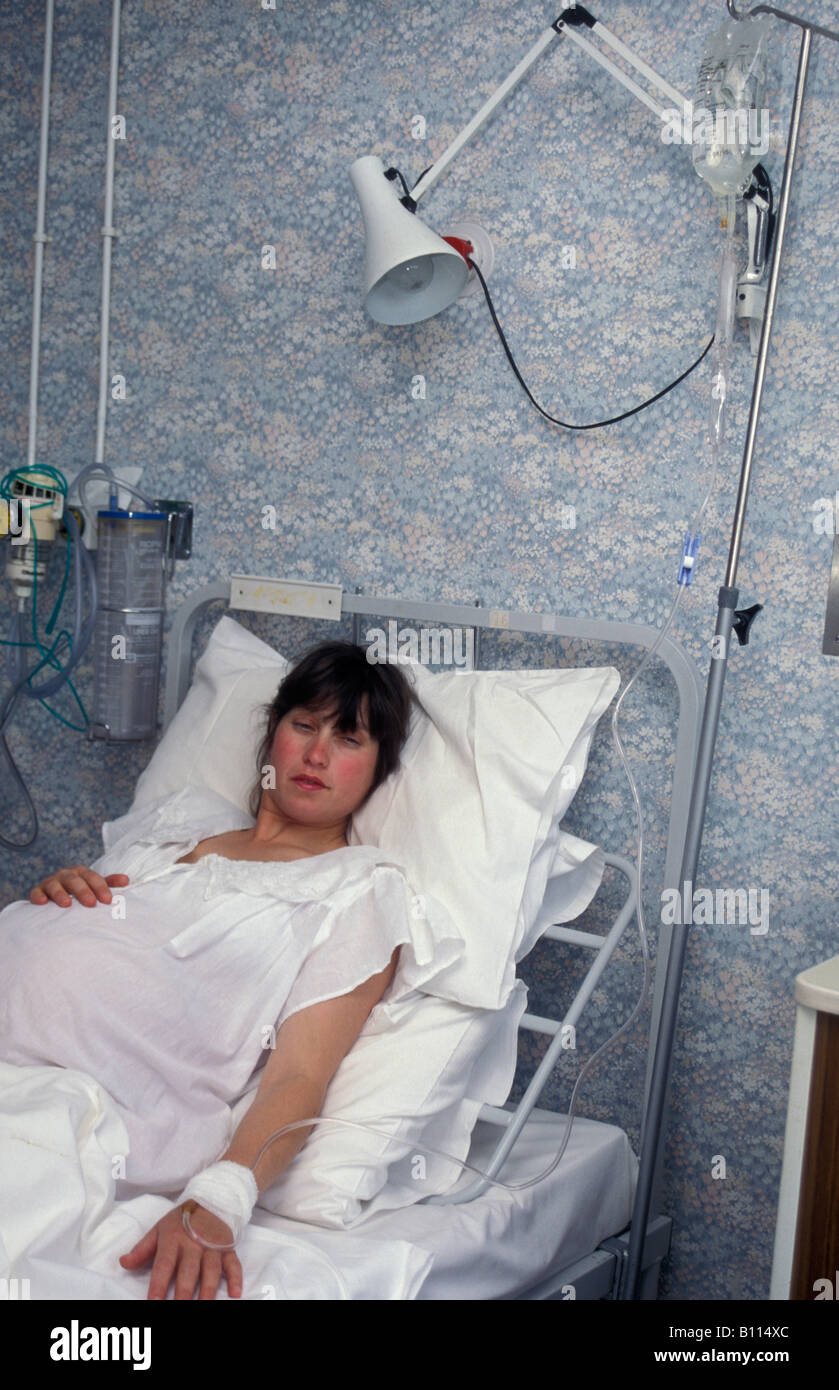 Giovane donna nel lavoro in ospedale giacente in letto attaccato al gocciolatoio Foto Stock