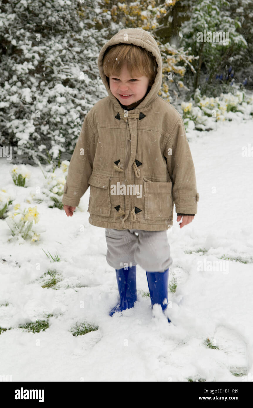 ragazzo, bambino, in piedi sulla neve vestito con abiti caldi che sembrano felici di essere fuori Foto Stock