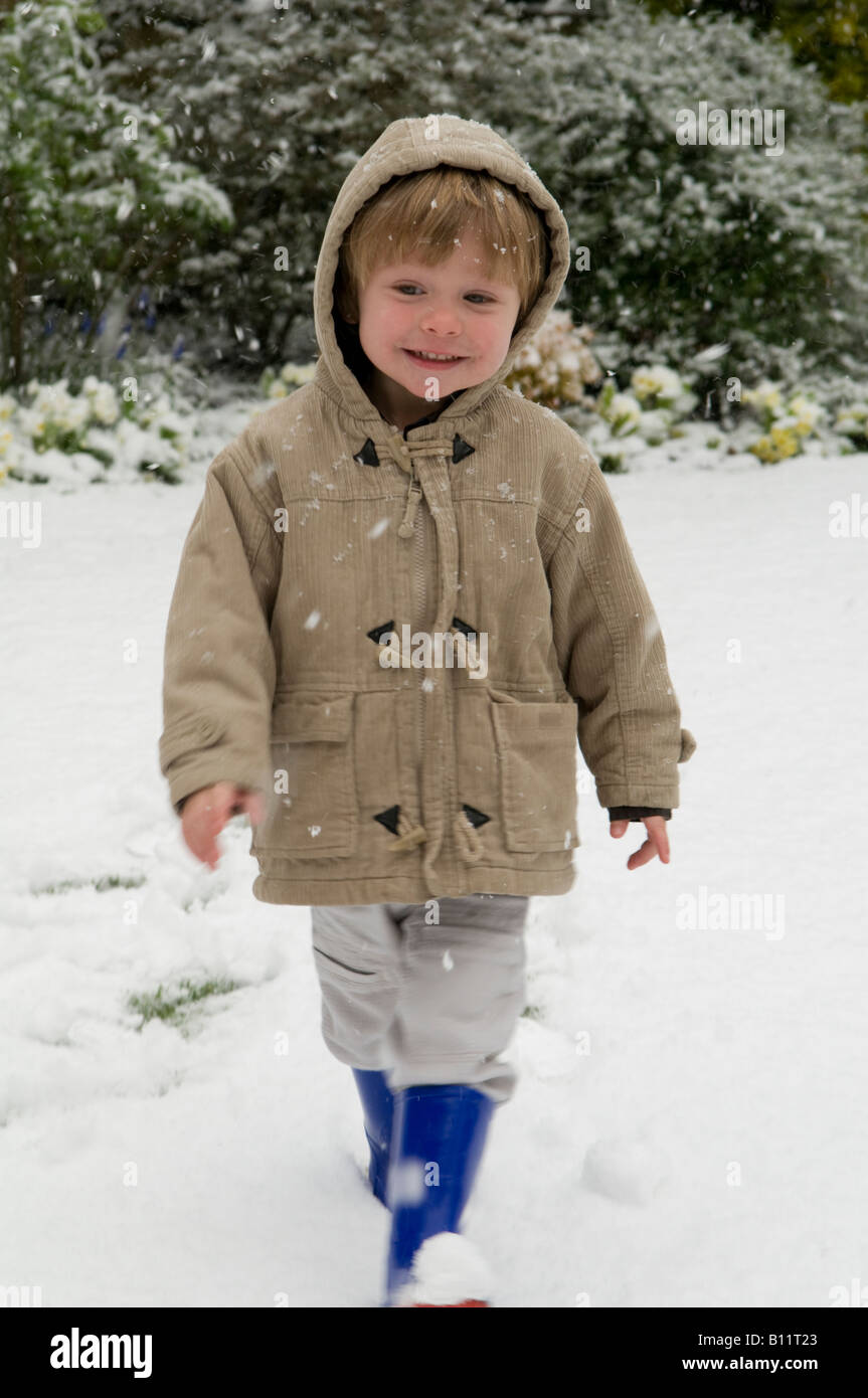ragazzo, bambino, in piedi sulla neve vestito con abiti caldi che sembrano felici di essere fuori Foto Stock