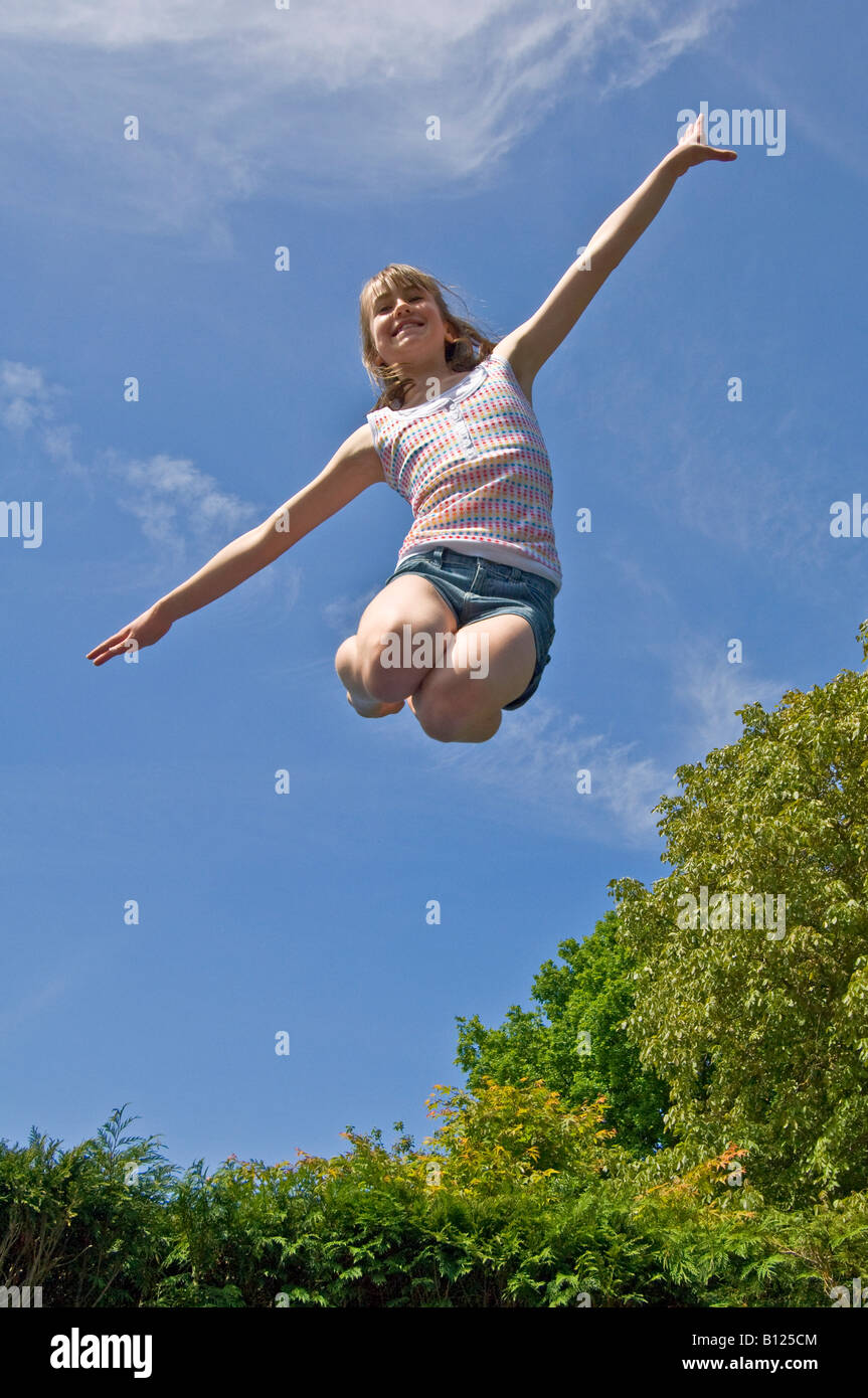 Una giovane ragazza (10 anni) che salta da un trampolino a metà in aria su un luminoso giorno di sole. Foto Stock