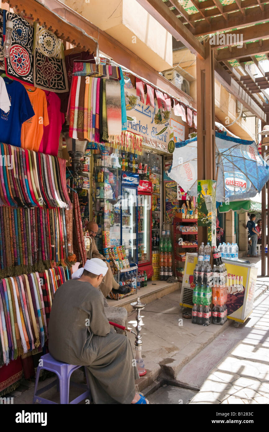 Negoziante locale fumare narghilè (o Waterpipe)nel bazaar nella sharia al Souk, Luxor, la Valle del Nilo, Egitto Foto Stock