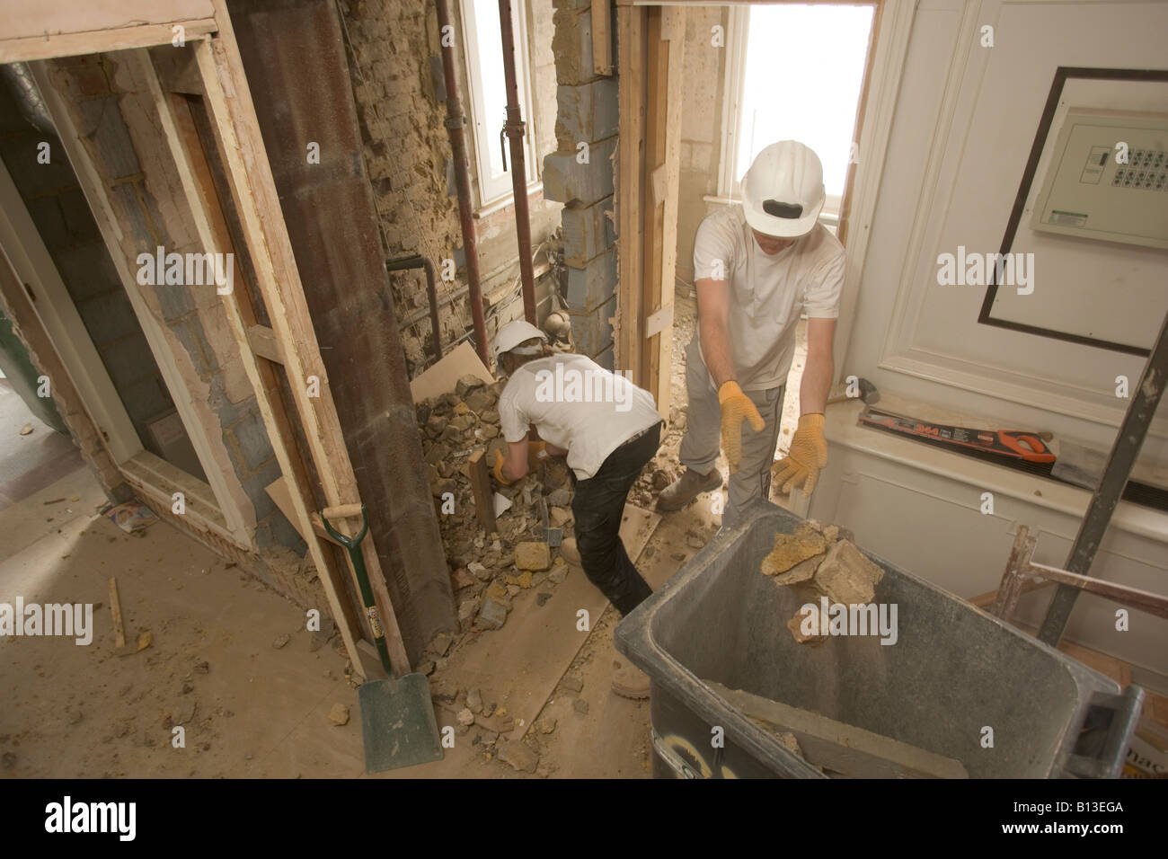 Un operaio getta macerie in un contenitore come il suo collega raccoglie più dal pavimento. Foto Stock