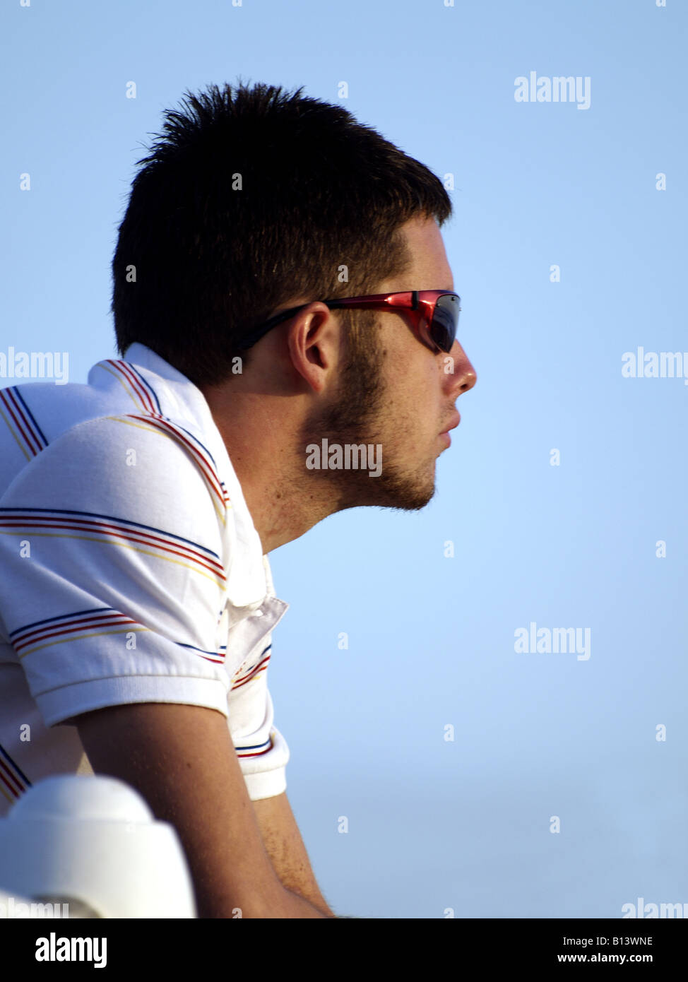 Vista laterale di un giovane uomo che indossa gli occhiali da sole, sostenuta da un cielo blu Foto Stock