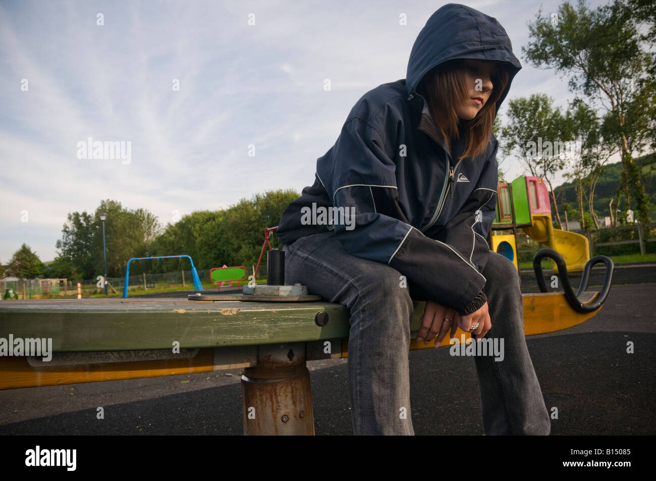 Un carattere introverso triste moody premuto ritirati ragazza adolescente seduto da solo in un parco giochi senza amici Foto Stock