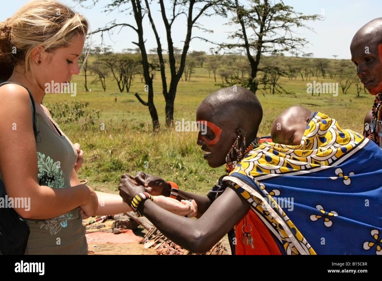 Masai Donna con bambino di vendita gioielli a una giovane donna britannica Foto Stock