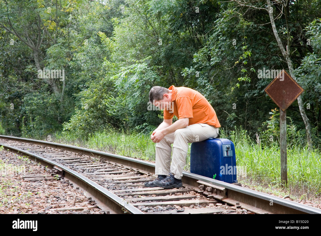 Uomo seduto sulla valigia su binari ferroviari Foto Stock