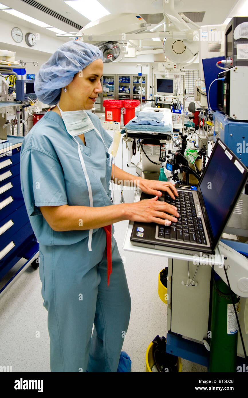 Prima di un intervento di una donna chirurgo indossando scrubs immette le informazioni pertinenti in una sala operatoria computer presso un ospedale Foto Stock