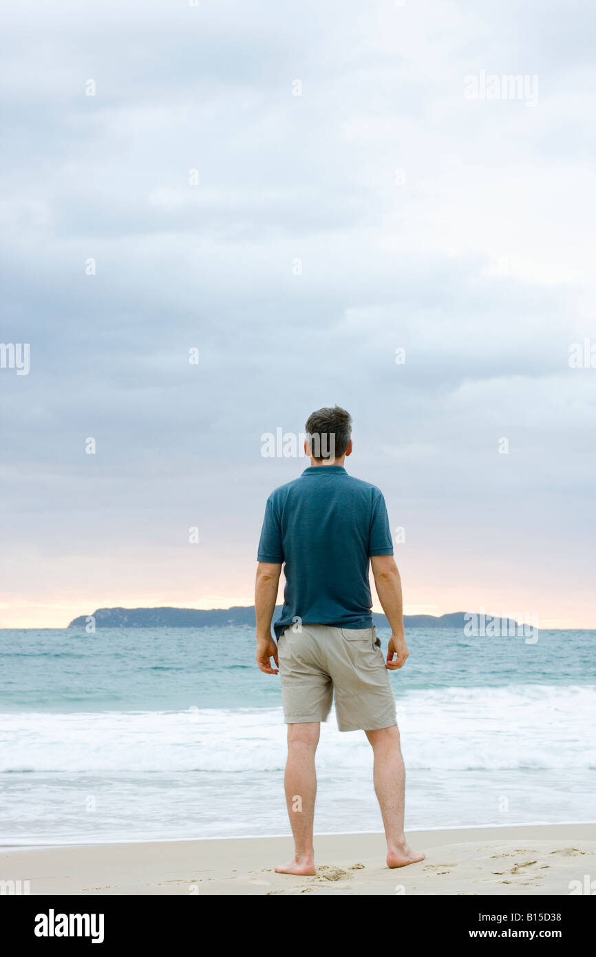Uomo in piedi sulla spiaggia contemplando il mare con un isola in background Foto Stock
