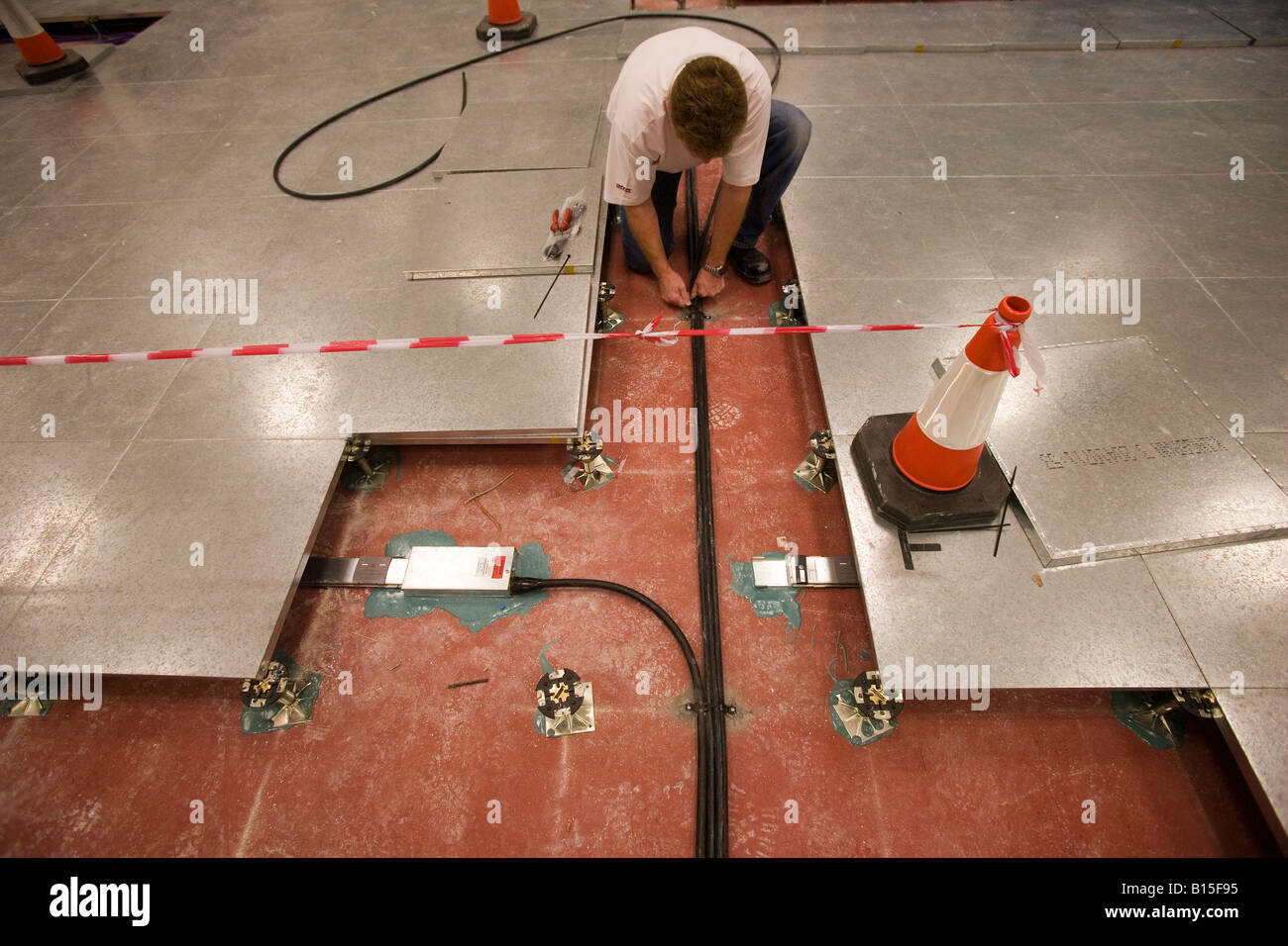 Un ingegnere appone sotto il pavimento di cablaggio di rete in un costruito di recente costruzione di ufficio. Foto Stock