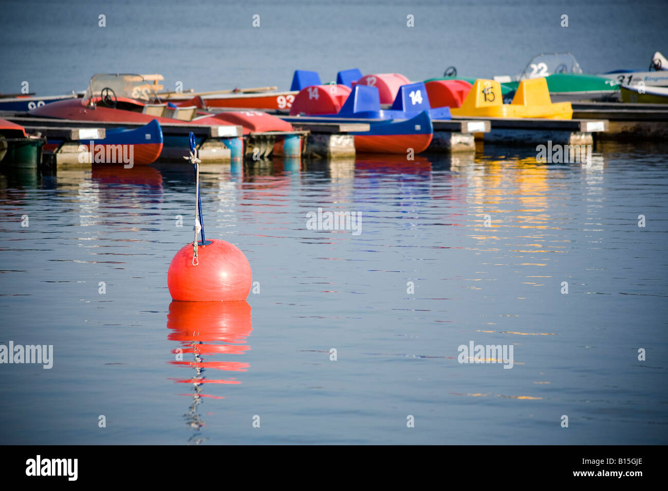 Colorato pedalò e canoe al molo sul lago, boa arancione in primo piano Foto Stock