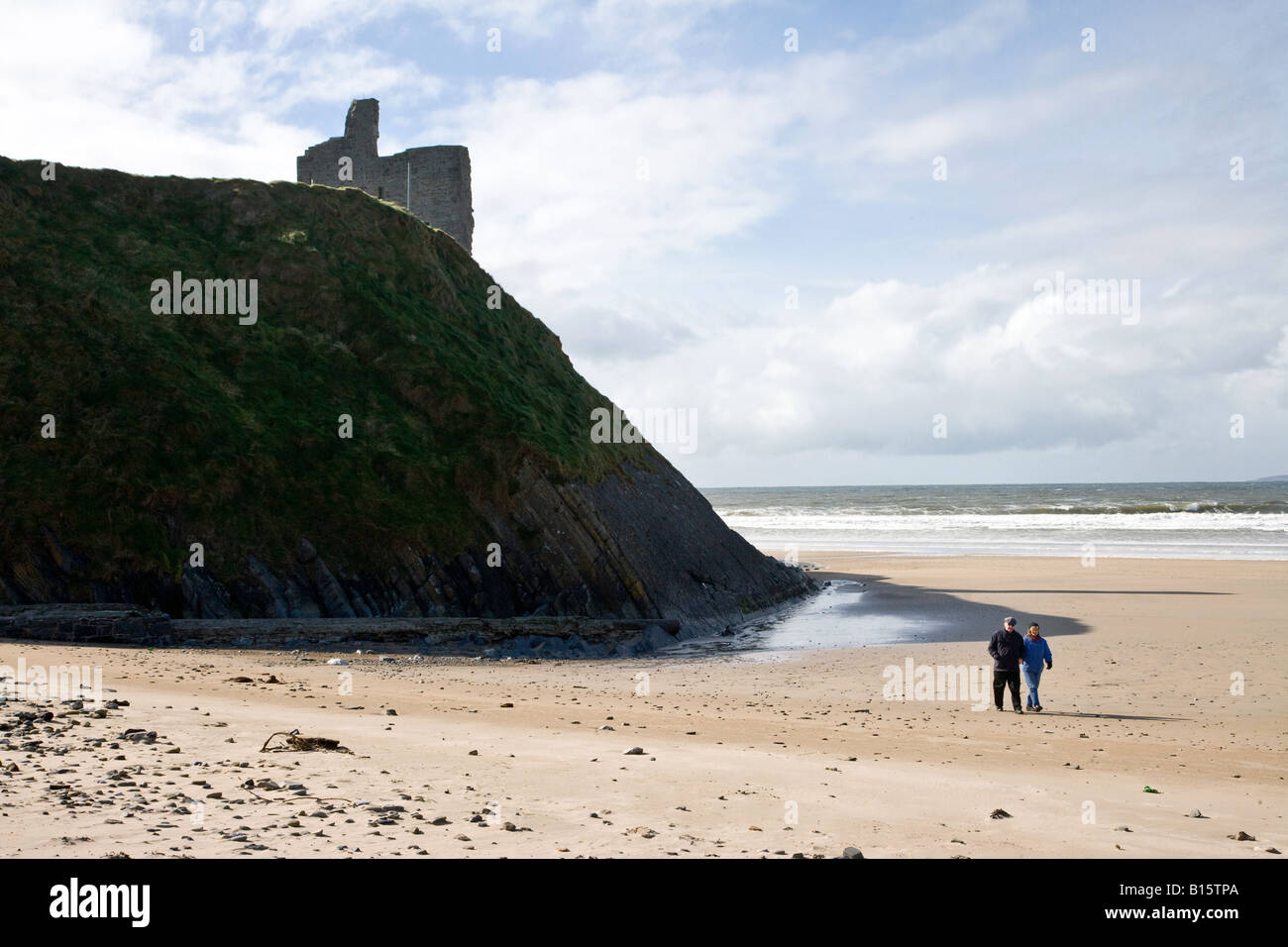 Giovane camminando sulla spiaggia vicino antico castello rovina sulla scogliera Ballybunnion Contea di Kerry, Irlanda Foto Stock