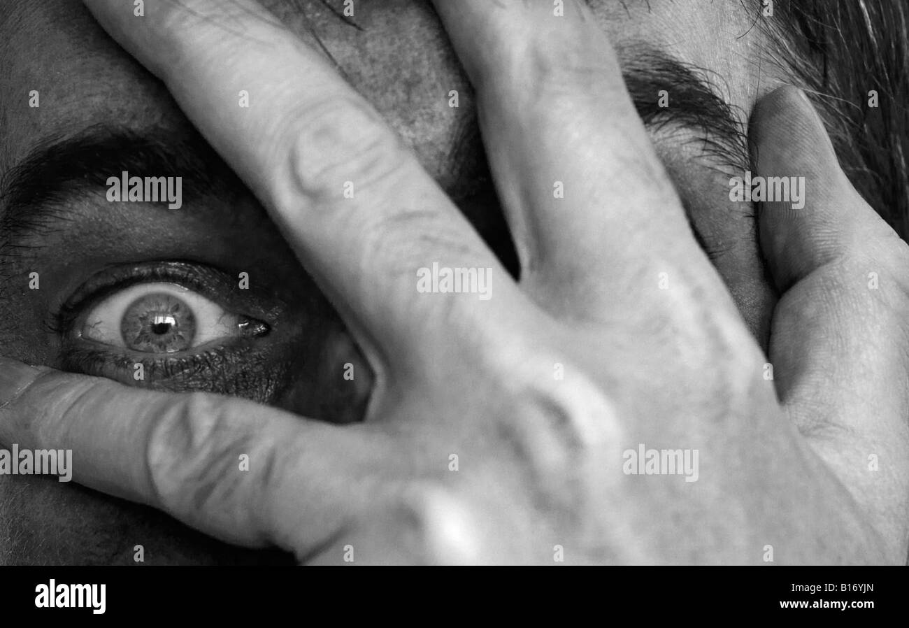 Uomo che ricopre la faccia con la mano guardando attraverso le dita Foto Stock