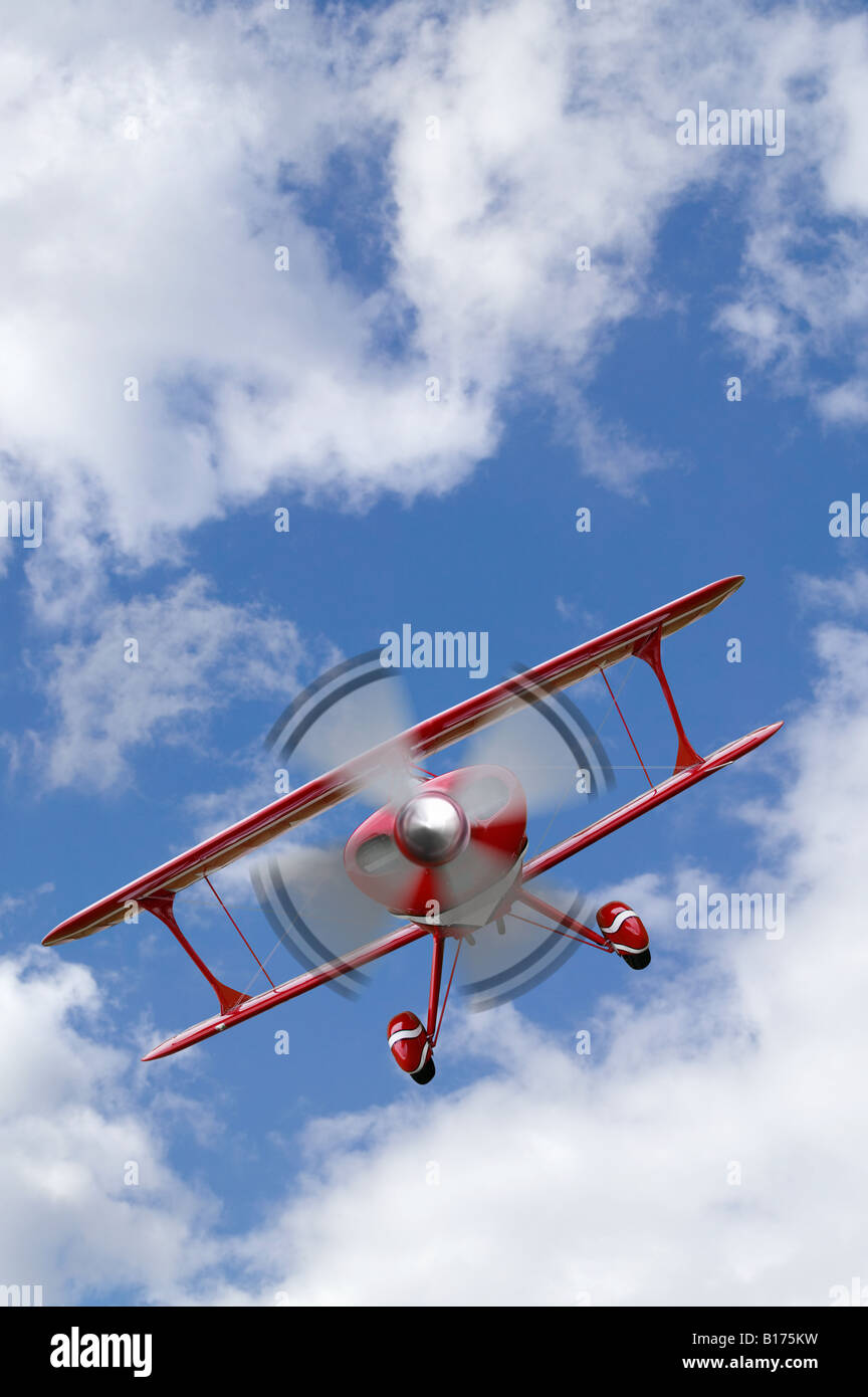Un biplano rosso battenti in un blu cielo nuvoloso Foto Stock