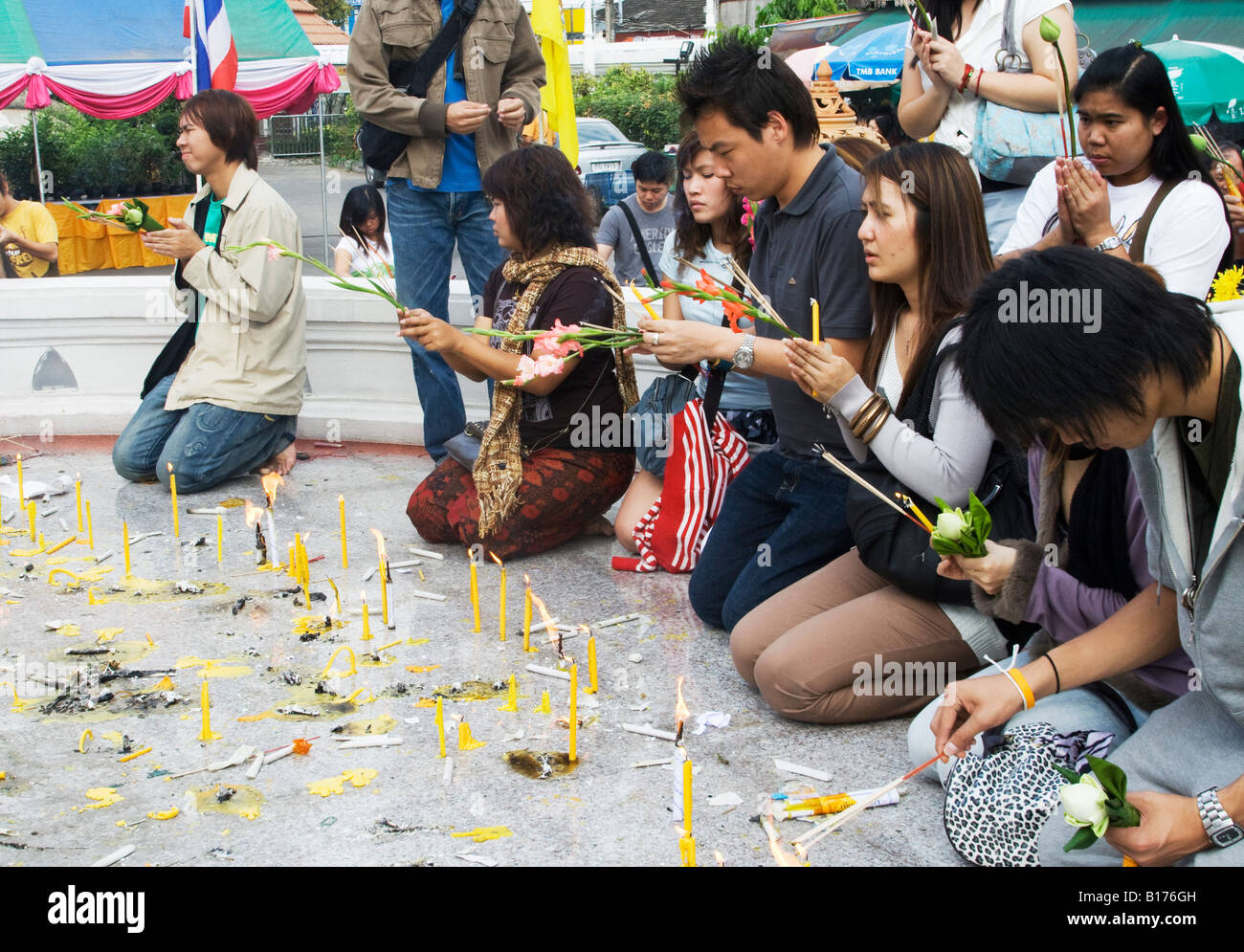 Un gruppo di persone si inginocchiano accendono le candele e pregare in un tempio buddista terreno Foto Stock
