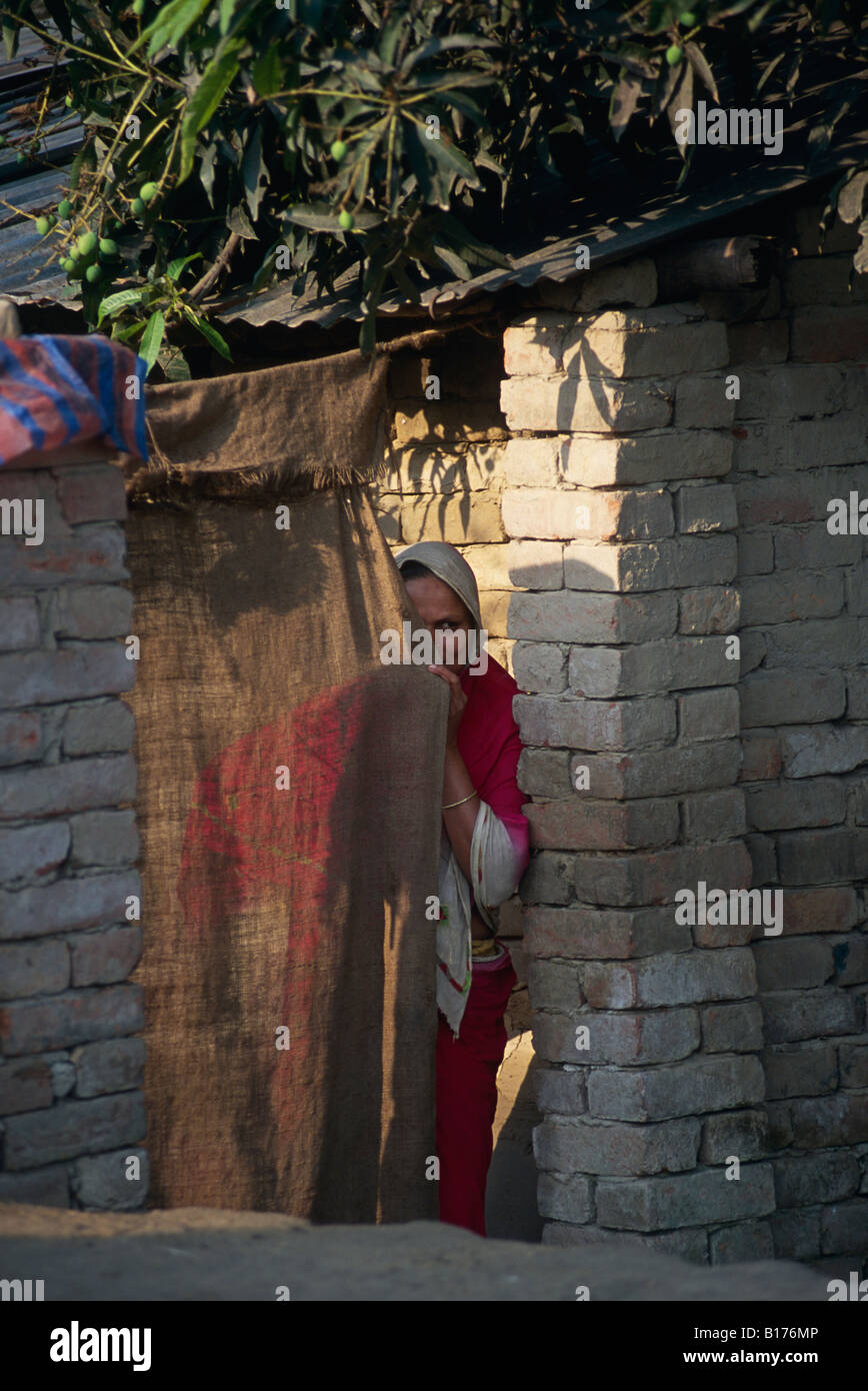 Donna del peering intorno a tendina Bangladesh Rural Village Foto Stock