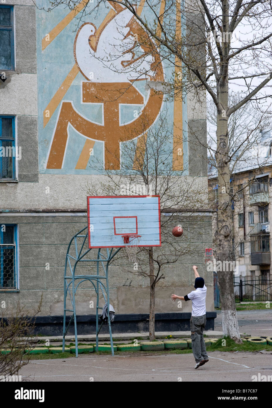 Ragazzo giocare a basket sulla corte nel vecchio era sovietica scuola con falce e martello murale di Yuzhno Sakhalinsk Sakhalin in Russia 2008 Foto Stock