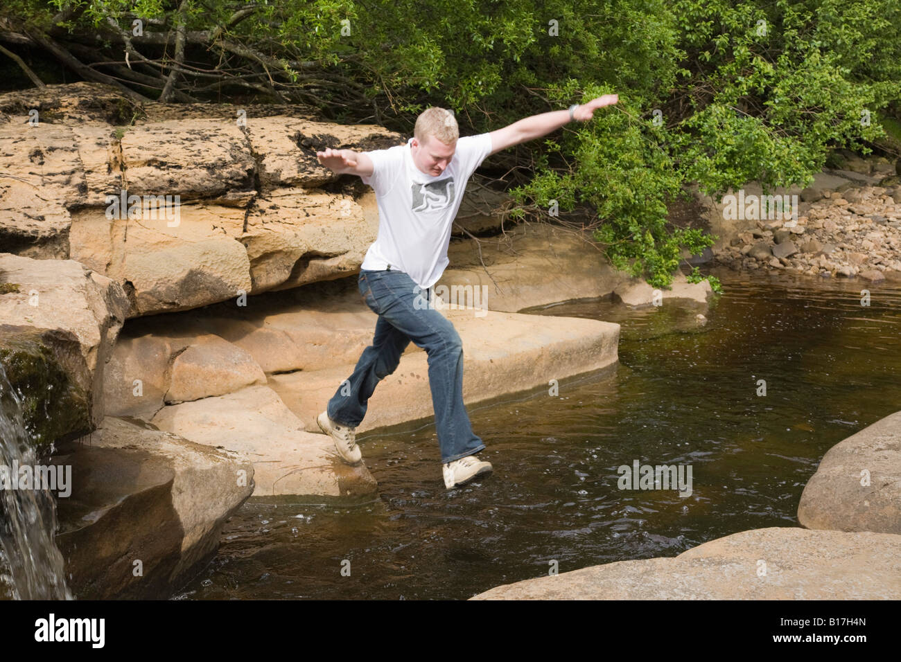 Un giovane uomo di saltare attraverso acqua in un fiume tra due rocce in Inghilterra, Regno Unito, Gran Bretagna Foto Stock