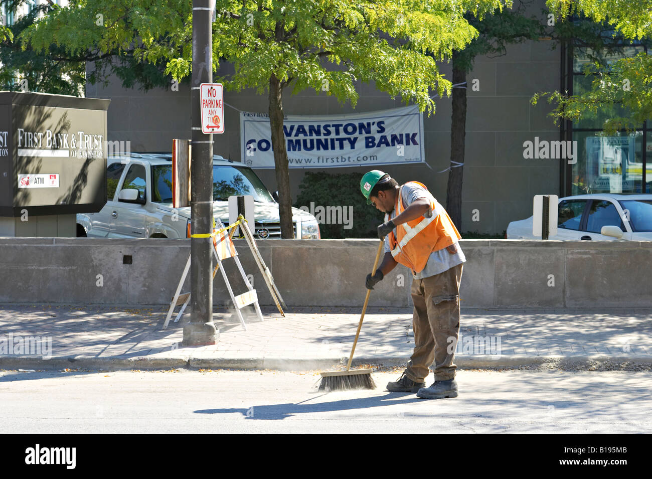Lavoratori Evanston in Illinois uomo sweep street nella zona di costruzione utilizzando push ginestra indossare elmetto arancione giubbotto di sicurezza Foto Stock