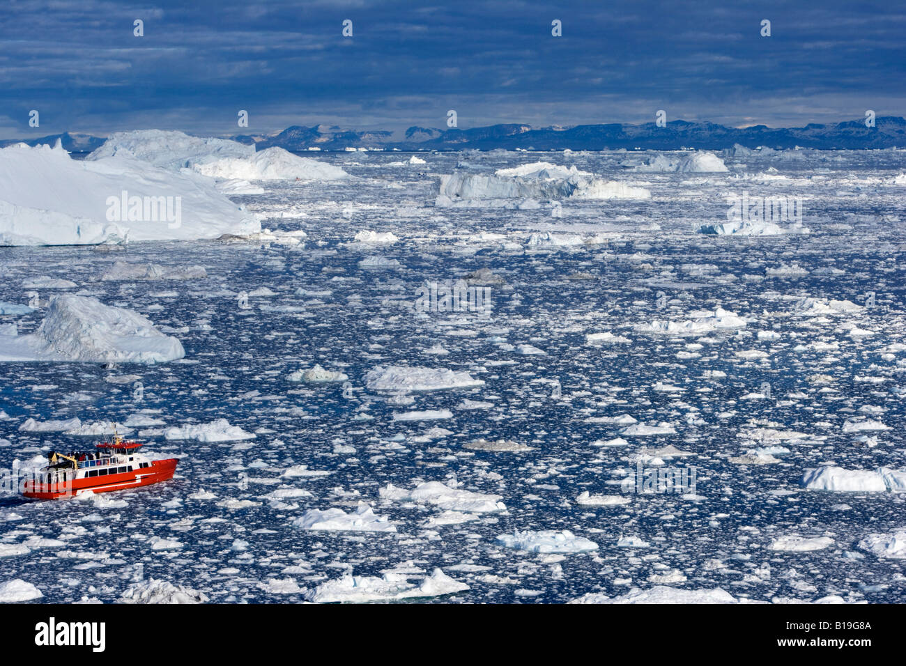 La Groenlandia, Ilulissat, Sito Patrimonio Mondiale dell'UNESCO icebergs. Una barca turistica naviga il suo modo attraverso il labirinto di iceberg. Foto Stock