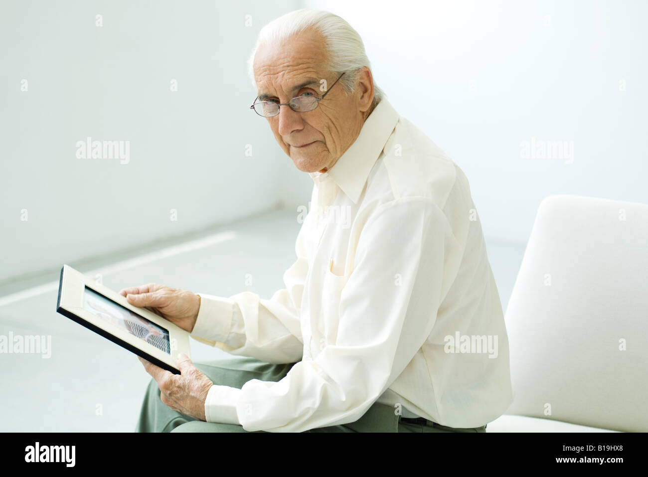 Senior uomo seduto, tenendo fotografia, guardando la fotocamera Foto Stock