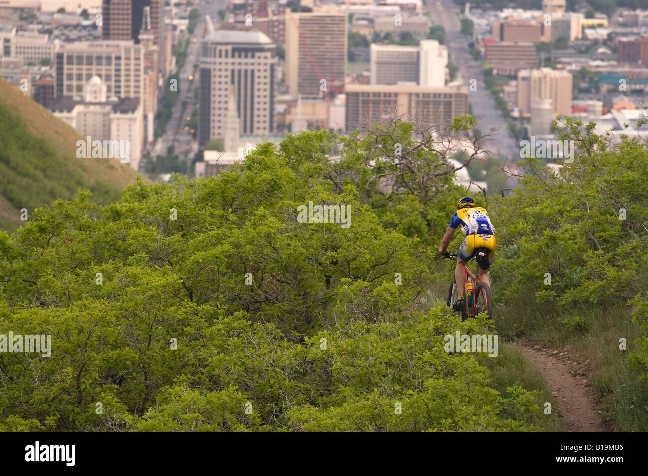 Un mountain biker scendendo un sentiero nelle colline sopra di Salt Lake City, Utah USA il centro città è visibile in background Foto Stock