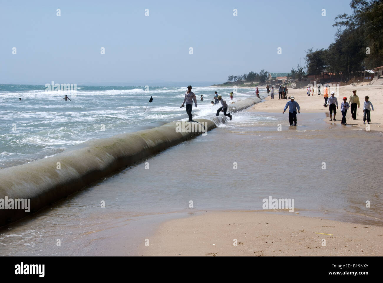 Le persone a rilassarsi passeggiando lungo le enormi sacchi di sabbia messo in atto per proteggere la restante area di spiaggia da ulteriore erosione Foto Stock