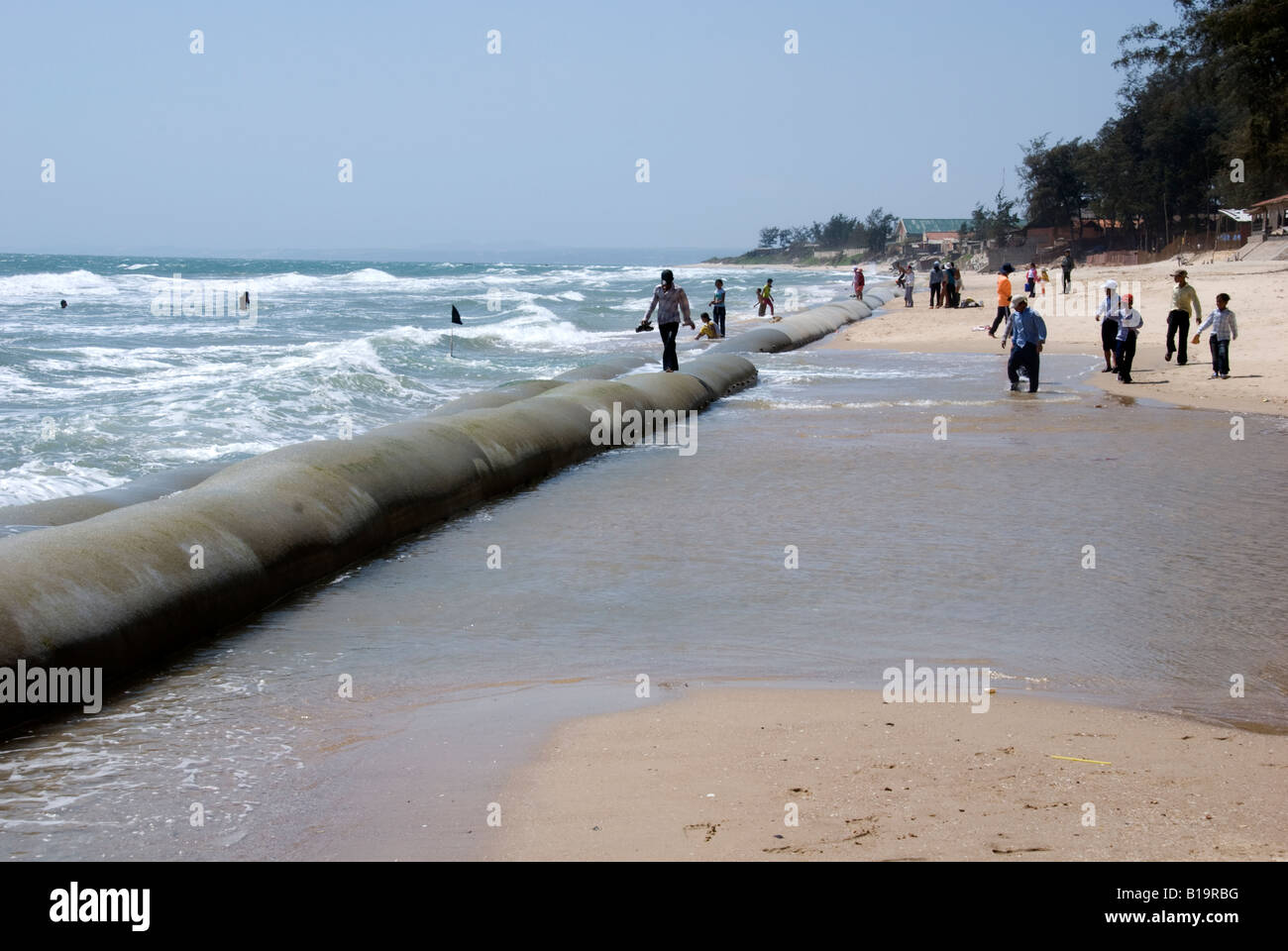 Le persone a rilassarsi passeggiando lungo le enormi sacchi di sabbia messo in atto per proteggere la restante area di spiaggia da ulteriore erosione Foto Stock