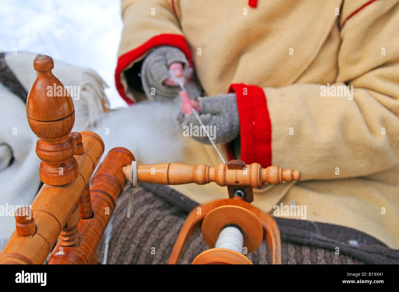 Rievocazione storica: una donna in lana costume invernale mano-la filatura della lana, in corrispondenza di un rustico snowy outdoor camp. Foto Stock