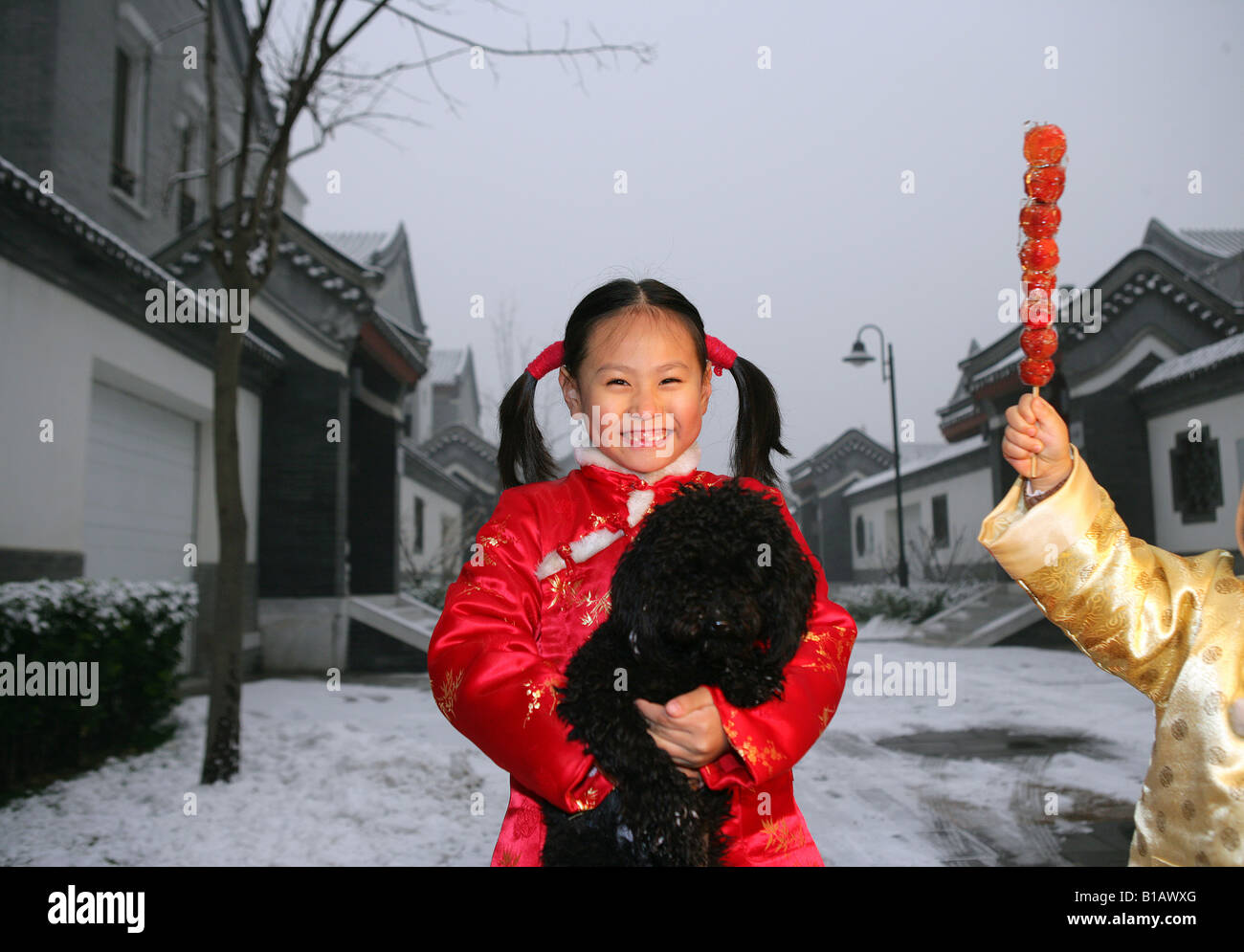 Due bambini cinesi a giocare con un cane nero nella neve Foto Stock