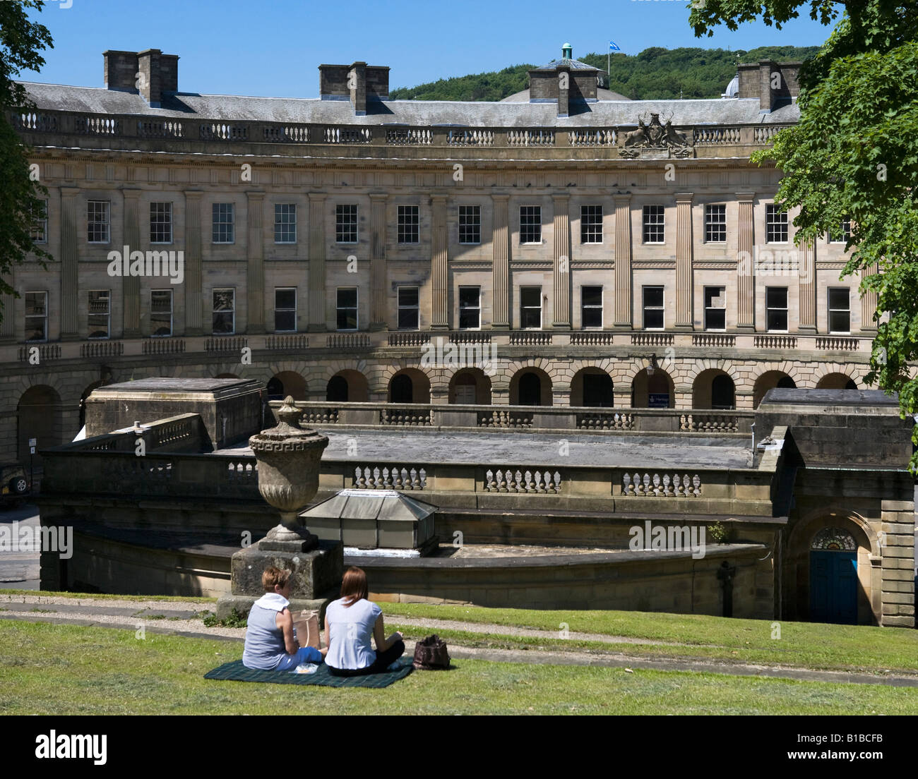 Due donne mangiare pranzo picnic che si affaccia sulla Crescent & camera della pompa, i pendii, Buxton, Peak District, Derbyshire, Inghilterra Foto Stock