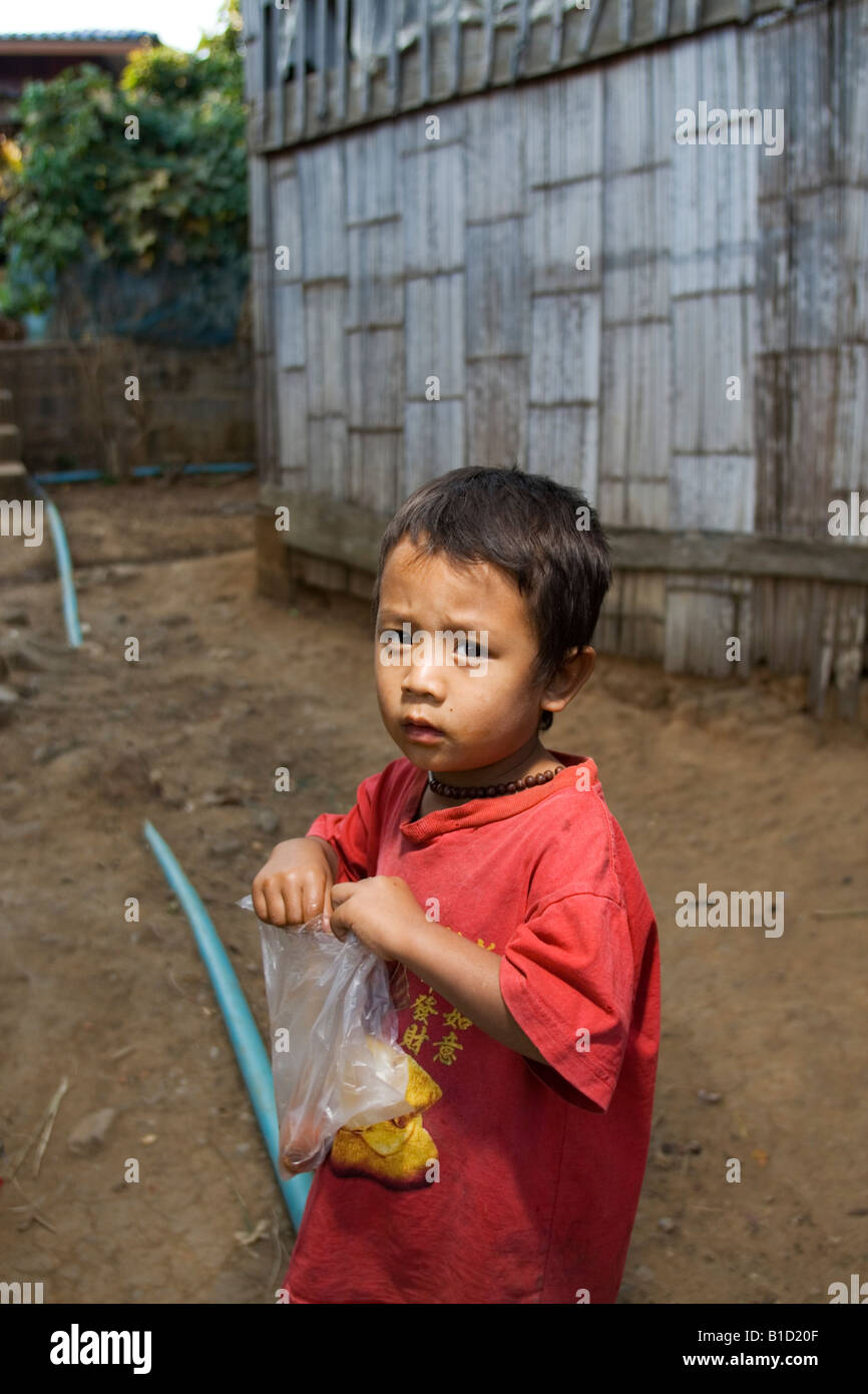 Un piccolo ragazzo dalla tribù Lisu nel nord della Thailandia con il cibo ha appena acquistato da un prodotto alimentare venditore ambulante Foto Stock
