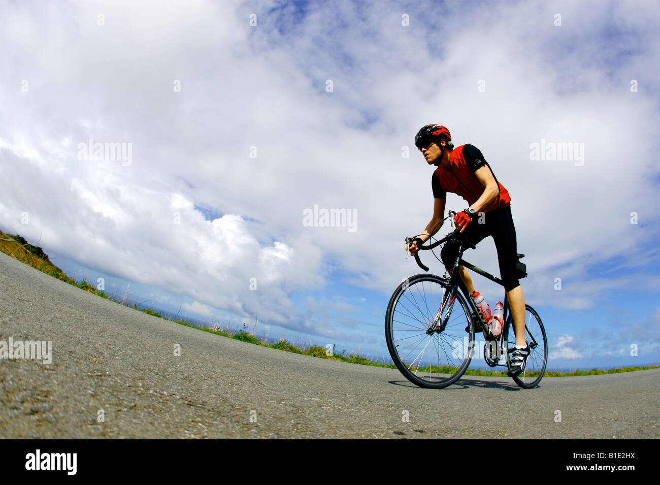 Un maschio ciclista, equitazione lungo la strada costiera in Cornovaglia su una bici da corsa Foto Stock