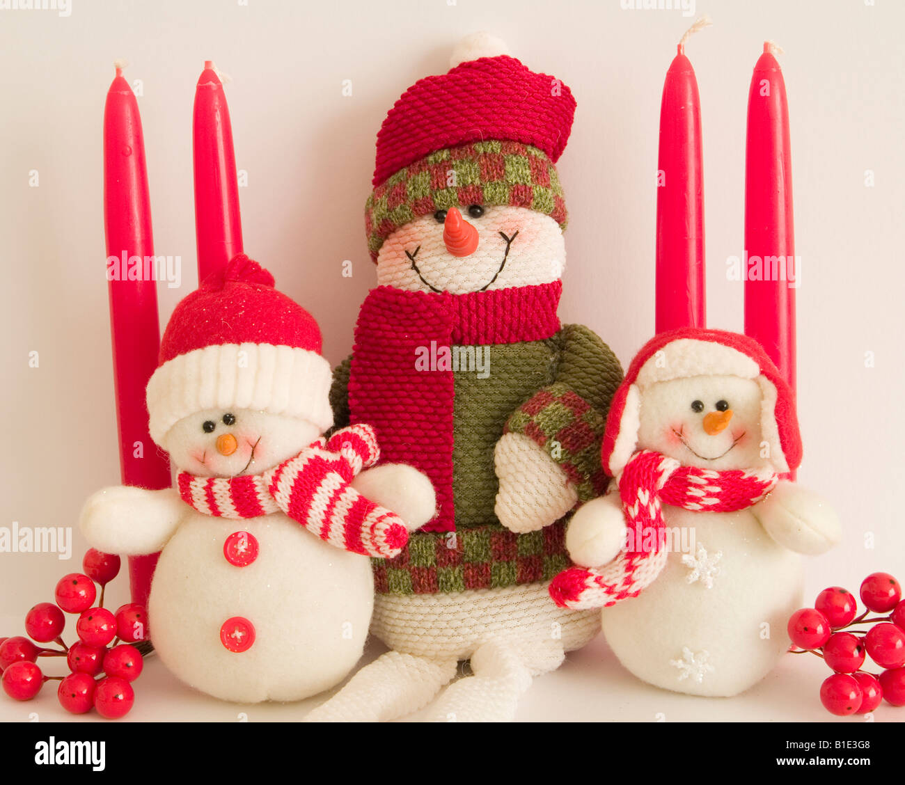 Tre pupazzi di neve a fianco a fianco con una disposizione di candele e bacche Foto Stock