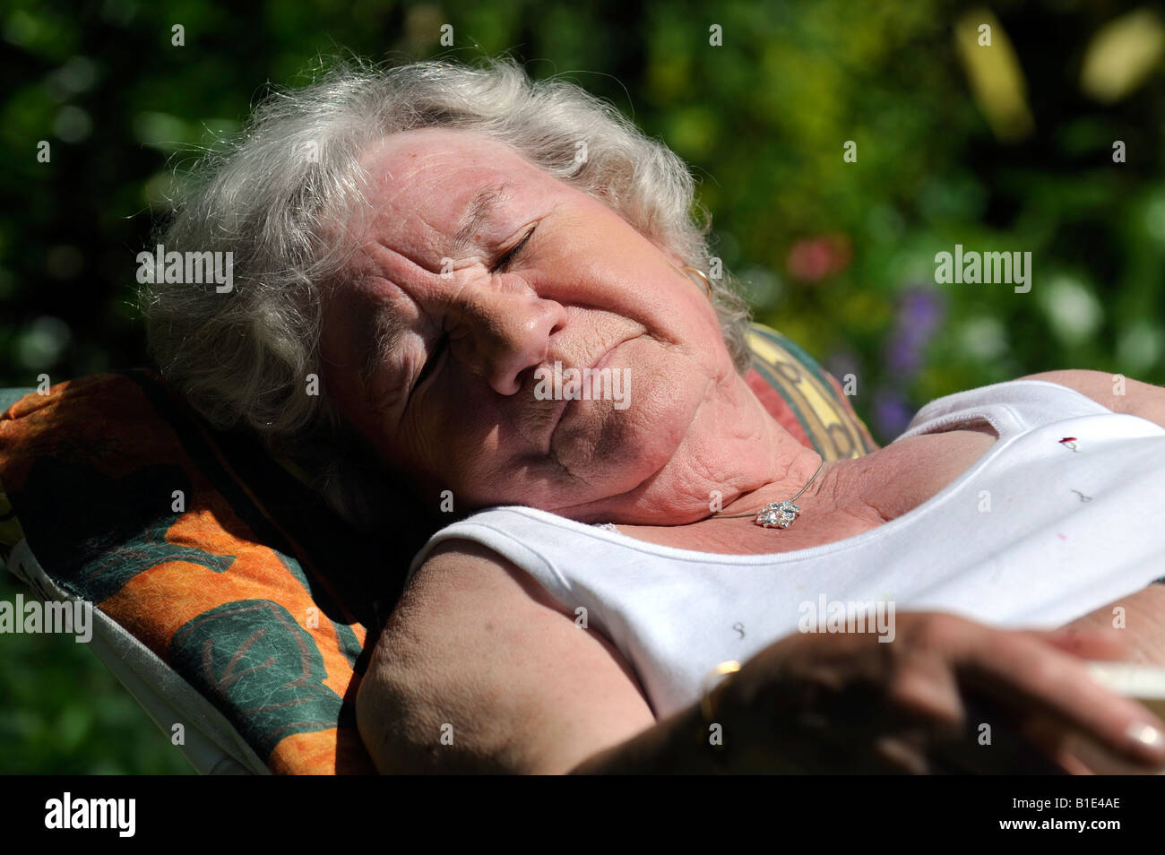 Una signora inglese titolare di pensione o di rendita gode di una posizione soleggiata giornata crogiolandovi al sole,UK,Inghilterra. Foto Stock