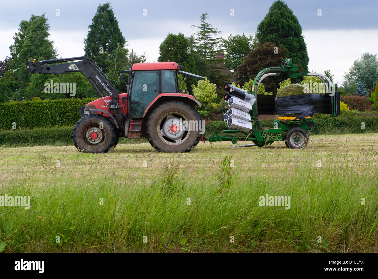 Rosso trattore McCormick tirando un wrapper di balla durante la fienagione in un campo di Cheshire Foto Stock