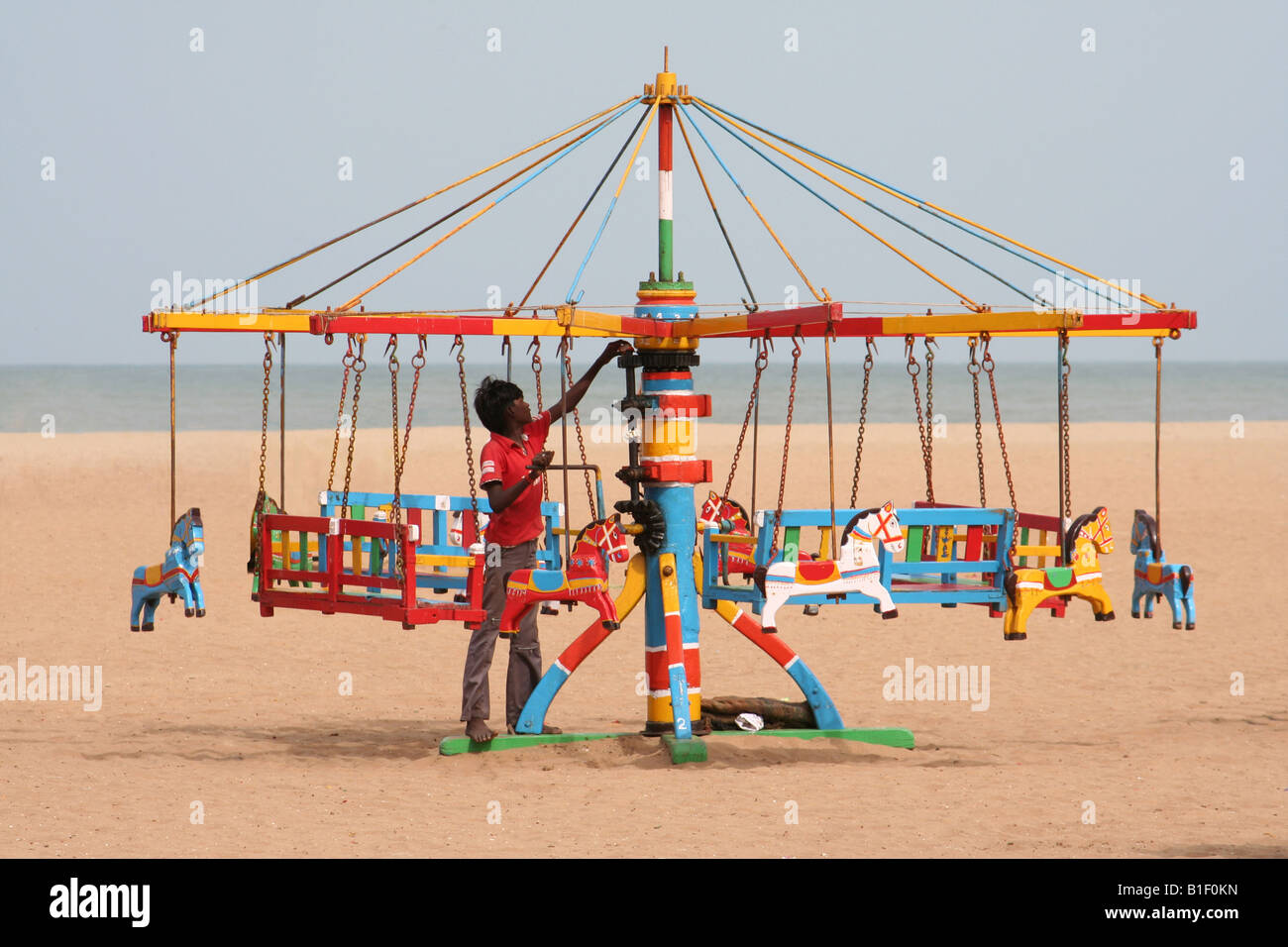Un indiano beach trader imposta la sua coloratissima giostra in legno nel tardo pomeriggio di sole Foto Stock