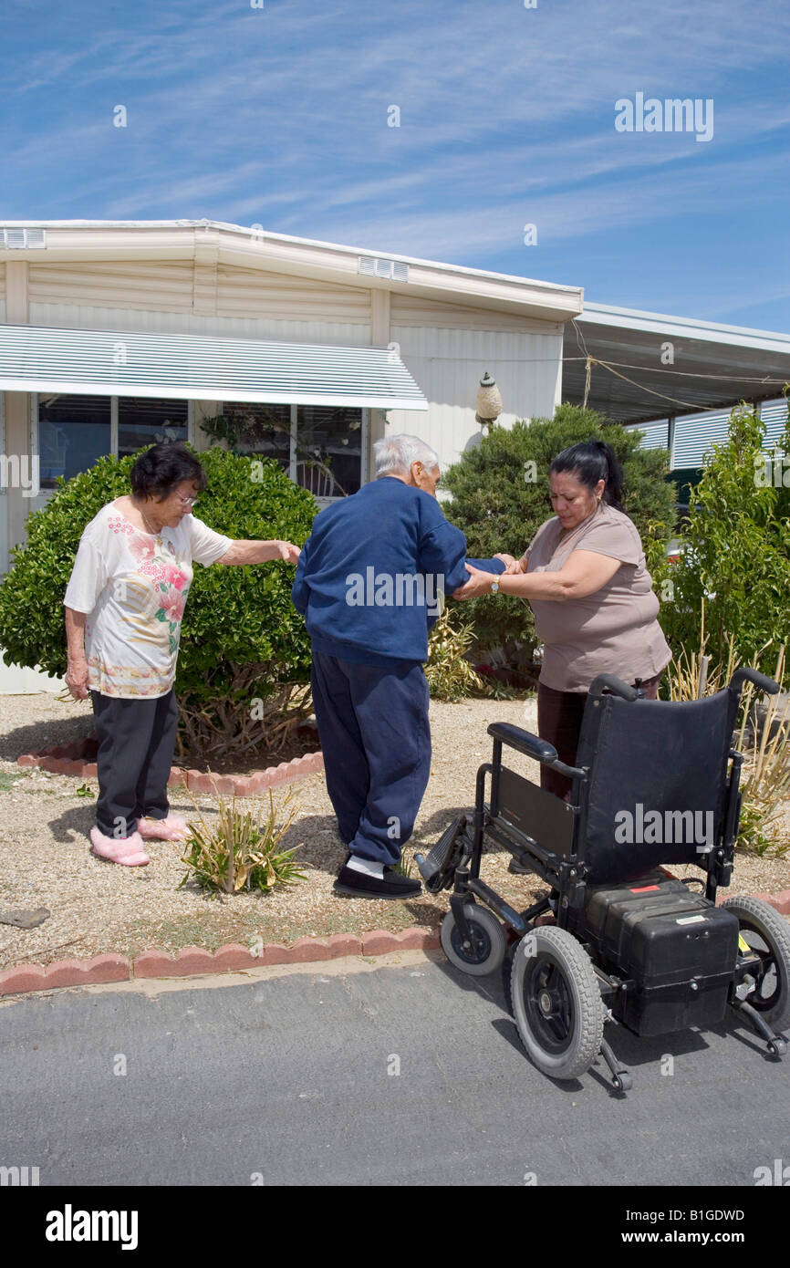 Donna ispanica aiuta il suo anziano padre getin in una sedia a rotelle come la sua mamma si affaccia su Foto Stock
