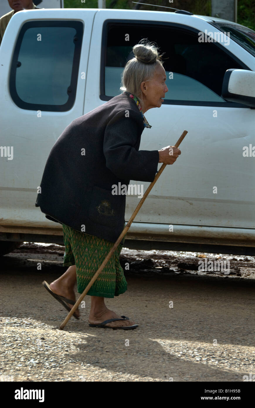 Vecchia donna camminare piegata con un bastone in un mercato nel nord della Thailandia Foto Stock