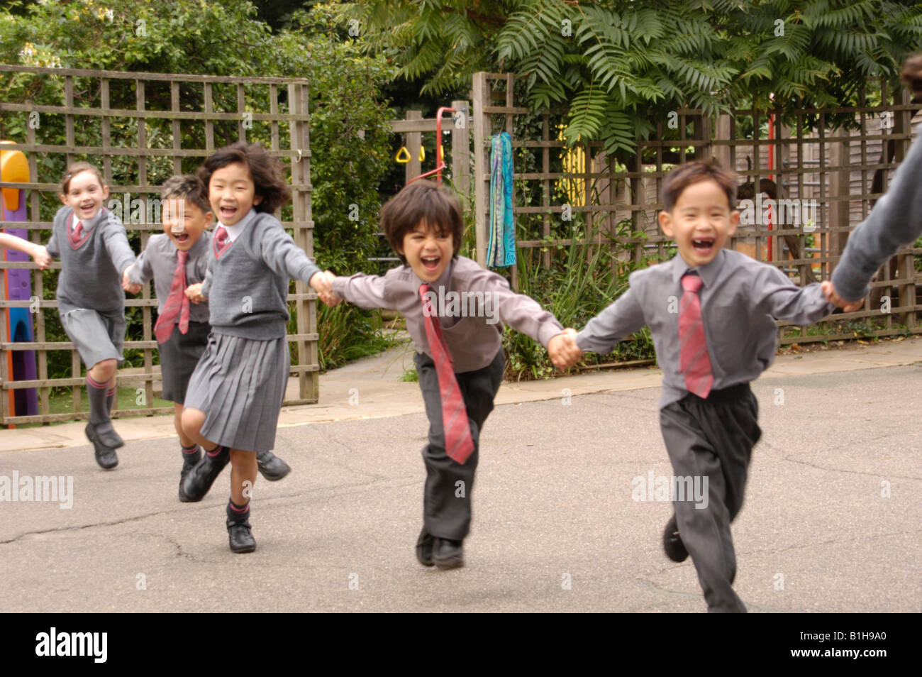 I bambini nel parco giochi di una scuola privata in esecuzione e tenendo le mani Foto Stock